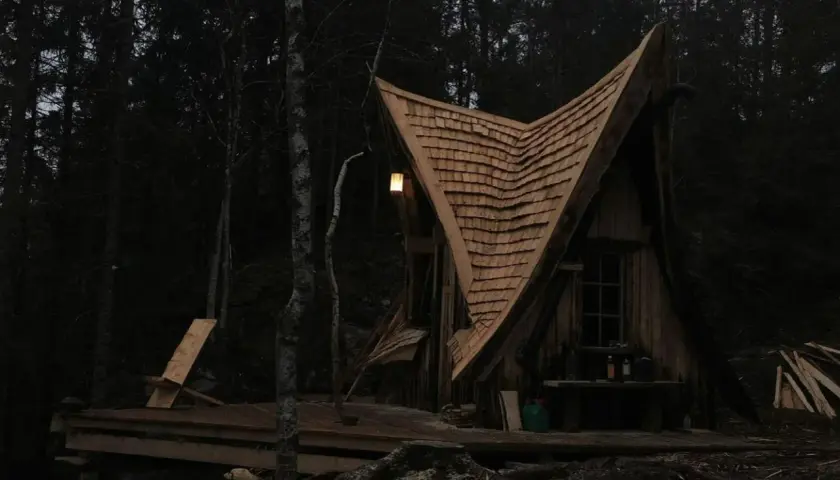 En magisk koja i skogen med ett spetsigt tak av träspån. En ensam stol står på altanen, redo för en stunds avkoppling.