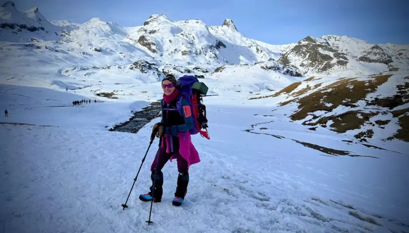 Una mujer con mochila y bastones disfruta de excursiones nieve en un paisaje montañoso cubierto de blanco.