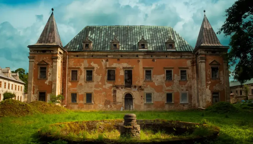 Zrujnowany pałac z wieżyczkami, porośnięty mchem i otoczony bujną zielenią. Kruszyna historii w zapomnianym miejscu.
