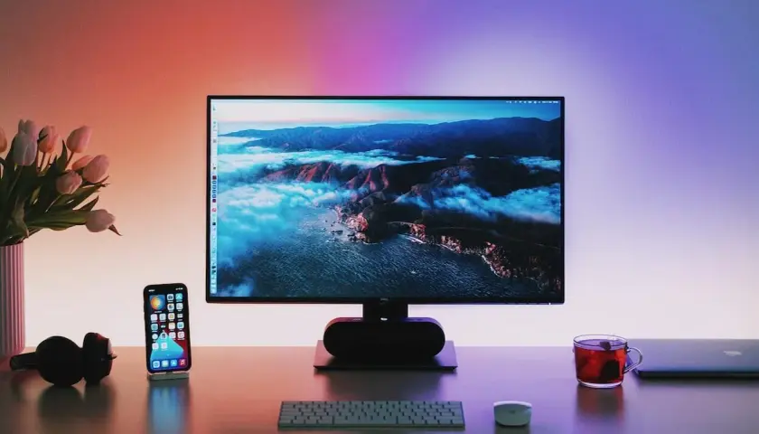 Biurko z telefonem, słuchawkami i klawiaturą. Na monitorze 144hz do 600 zł krajobraz górski.