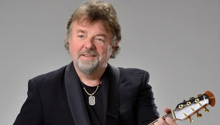 Mariusz Kalaga w czarnym garniturze gra na gitarze.