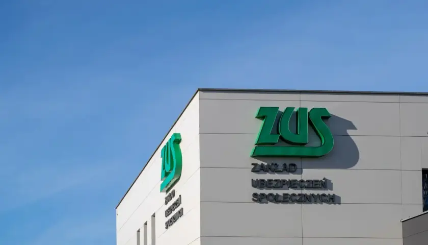 Budynek ZUS z zielonym logo i napisem "Zakład Ubezpieczeń Społecznych" na tle błękitnego nieba.
