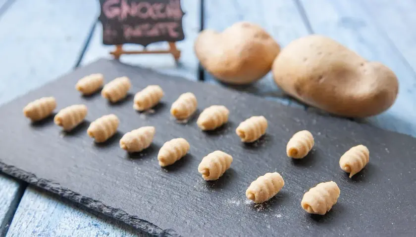 Gnocchi fatti in casa, morbidi e rigati, pronti per essere cucinati. Due patate sullo sfondo, ingredienti freschi per un piatto delizioso.