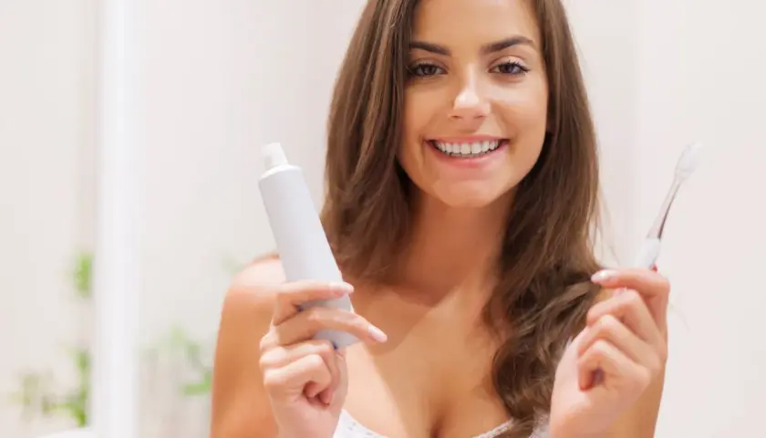 Donna sorridente con dentifricio e spazzolino. Controlla sempre la data di scadenza, perché il dentifricio scade!