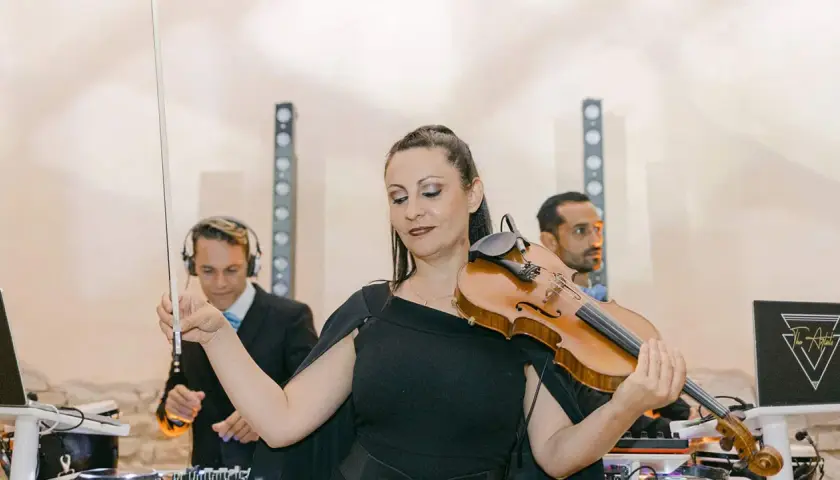 Une violoniste joue lors d'un mariage, avec des DJs en arrière-plan. Un prix DJ mariage pour une ambiance unique.