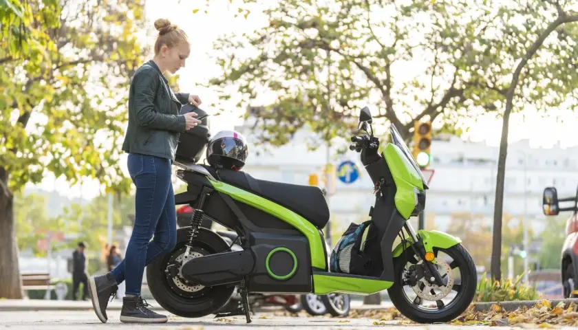 Mujer con casco y móvil junto a ciclomotor eléctrico verde. ¿Cuál será su velocidad máxima?