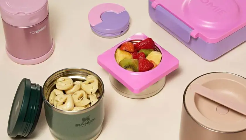 Colorful bento boxes and insulated food jars filled with pasta and fruit. These containers are designed to keep food warm for lunch.