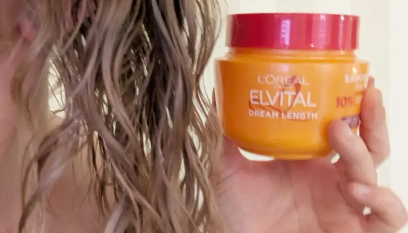 En hand håller en burk med L'Oréal Elvital Dream Length hårinpackning bredvid blekt, vått hår.