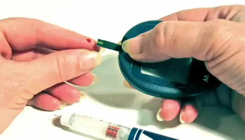 Kropla krwi na palcu, pasek testowy i glukometr. Obok wstrzykiwacz z insuliną aspart sanofi.