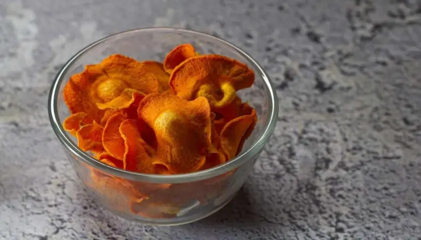 Croccanti chips di carote, preparate in friggitrice ad aria, servite in una ciotola di vetro.
