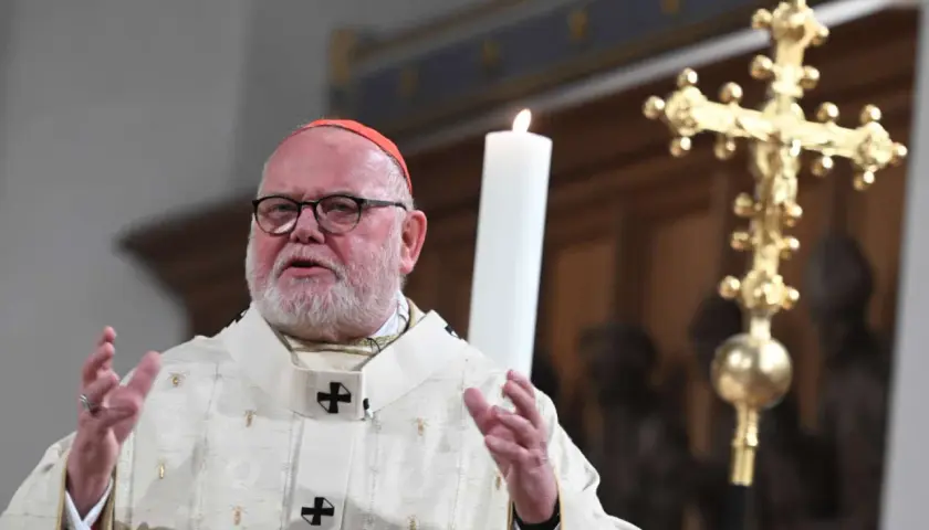 Kardinal Marx spricht in festlicher Robe vor einer Kerze und einem goldenen Kreuz.