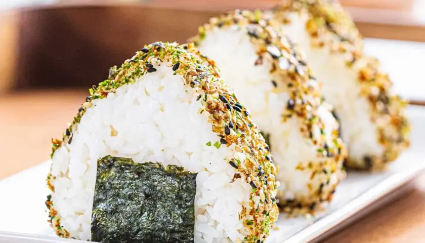 Triangular onigiri rice balls, coated in furikake seasoning, showcase the best rice for onigiri. A piece of nori seaweed adorns the front.