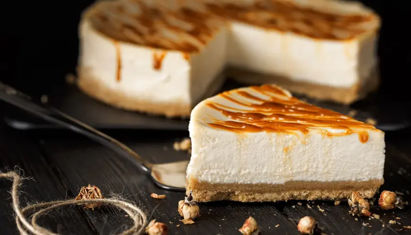 Una fetta di cheesecake fredda senza gelatina, con glassa al caramello, su un piatto scuro.