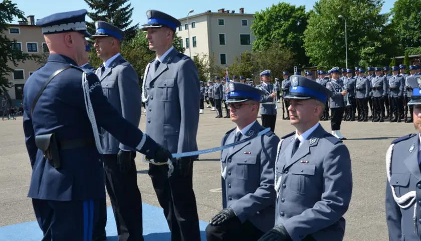 Uroczyste mianowanie na nowych zasadach. Policjanci w galowych mundurach, jeden klęczy, otrzymując szablę.