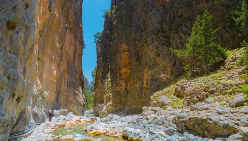 Wanderer in der Samaria Schlucht, umgeben von steilen Felswänden und einem klaren Flussbett.