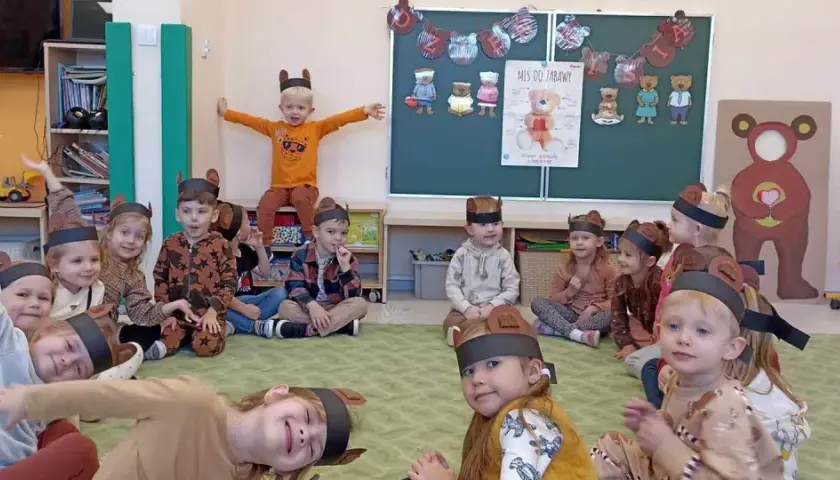 Dzieci w strojach misiów siedzą na dywanie w sali przedszkolnej.