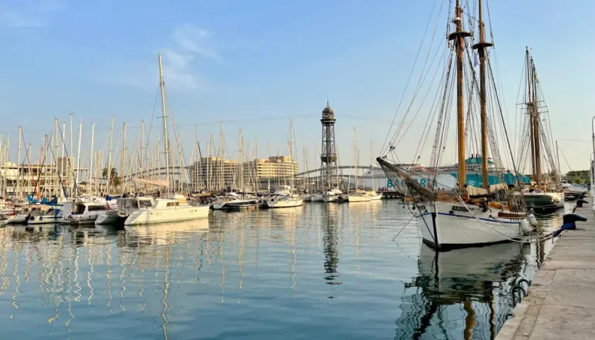 Port w Barcelonie z żaglówkami i wieżą widokową w tle.