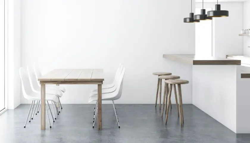 Tavolo in legno con sedie bianche e sgabelli al bancone, su un elegante **pavimento senza fughe**.