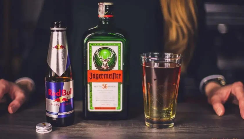 Butelka Red Bull i Jägermeister obok szklanki z drinkiem. Idealny zestaw na imprezę.