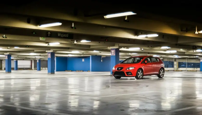 Czerwony samochód na pustym parkingu podziemnym. W tle tablica "Wyjazd". Myśląc o opłatach za garaż we wspólnocie mieszkaniowej, warto pamiętać o takich miejscach.