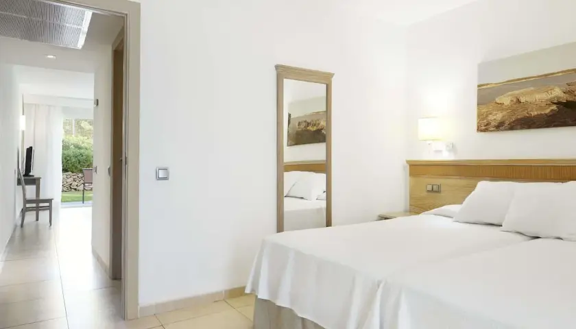 Habitación luminosa en Iberostar Club Cala Barca con dos camas, espejo de cuerpo entero y acceso a un patio exterior.