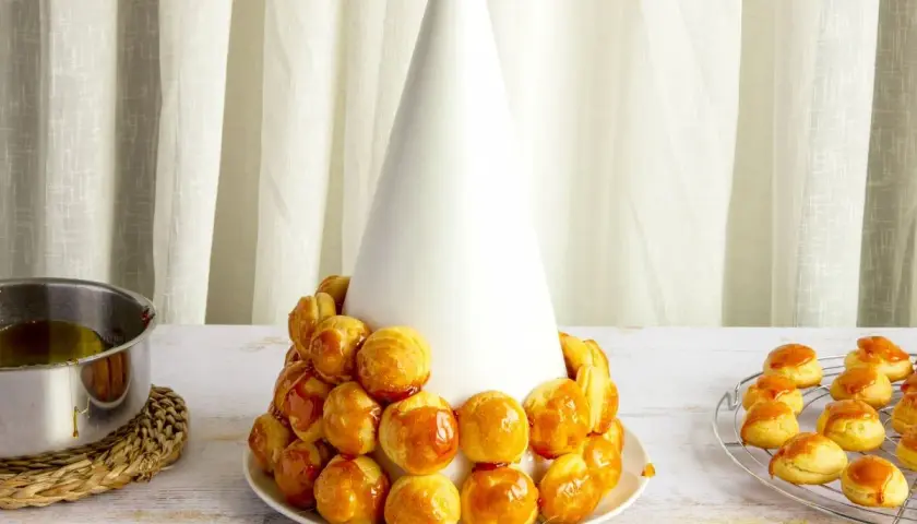 Tarta de profiteroles en proceso, con los pastelitos dorados y brillantes, listos para ser cubiertos de caramelo.