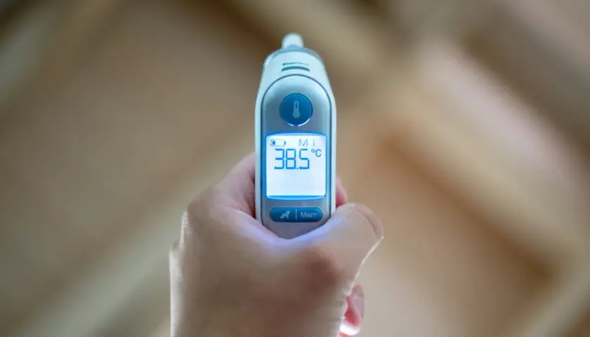 Dłoń trzyma termometr wskazujący 38.5°C. To 39 stopni gorączki u dorosłego, czas na odpoczynek i leki.