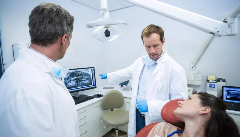 Dwóch dentystów omawia zdjęcie rentgenowskie z pacjentką, zastanawiając się, ile zarabia dentysta NFZ.