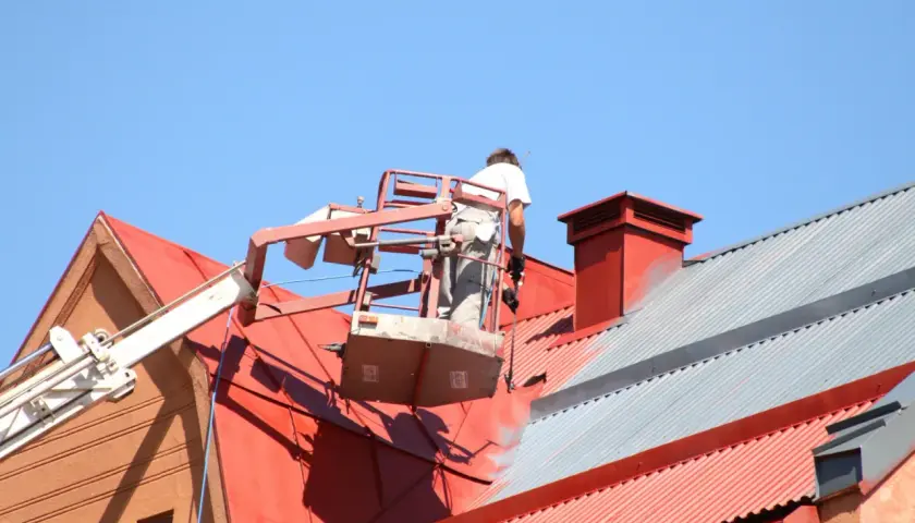 Pracownik na podnośniku maluje czerwony dach. Sprawdź, jaka jest malowanie dachu cena i odśwież wygląd swojego domu.
