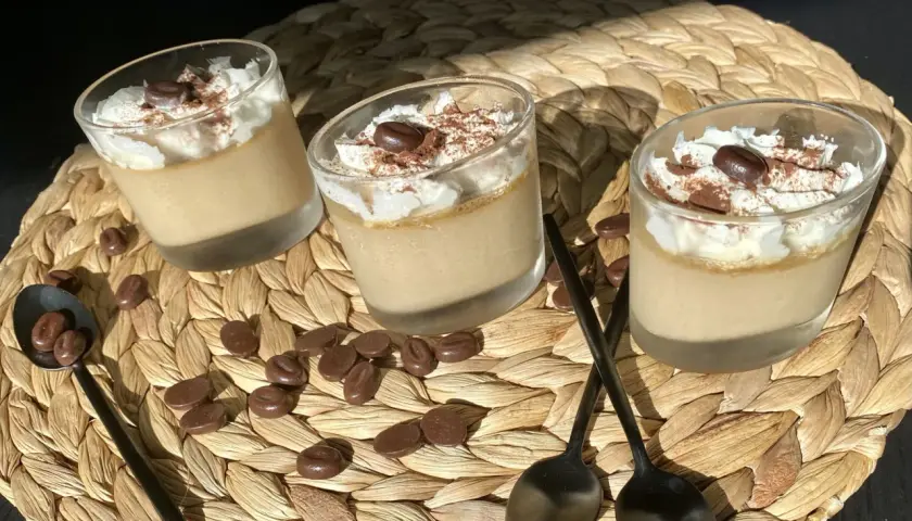 Trois verrines de crème au café facile, garnies de chantilly, cacao et grains de café. Des chocolats en forme de grains parsèment le napperon.