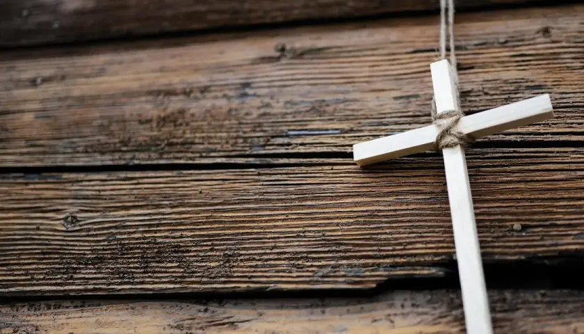 Ein hölzernes Kreuz, gebunden mit Seil, hängt vor einer rustikalen Holzvertäfelung. Ein Symbol für den Karfreitag, den Feiertag der Besinnung.