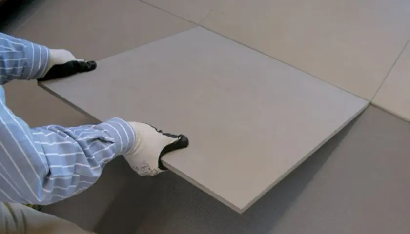 Mani guantate posizionano una piastrella su un pavimento in fase di posa.