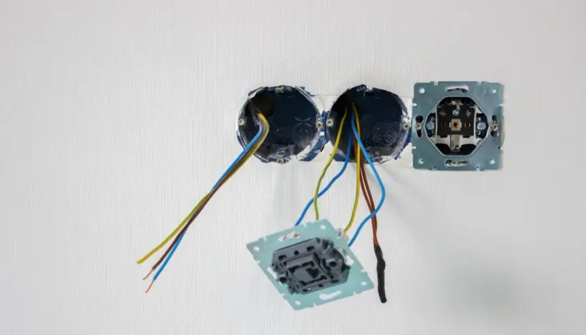 Instalacja elektryczna: puszki, przewody i mechanizmy gniazdek na białej ścianie.