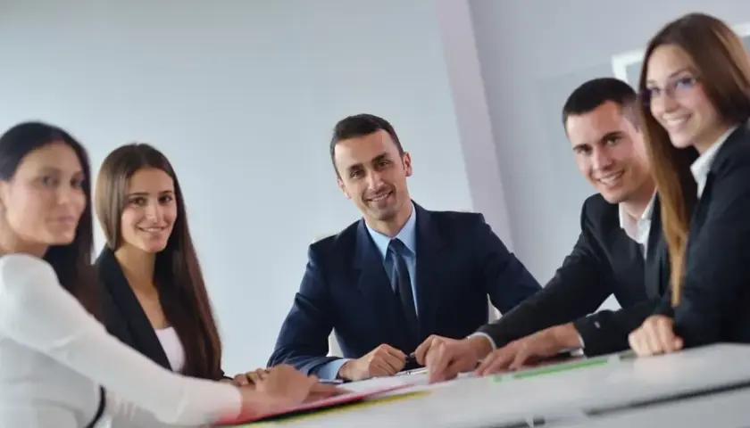 Grupa ludzi w garniturach siedzi przy stole, dyskutując nad dokumentami.