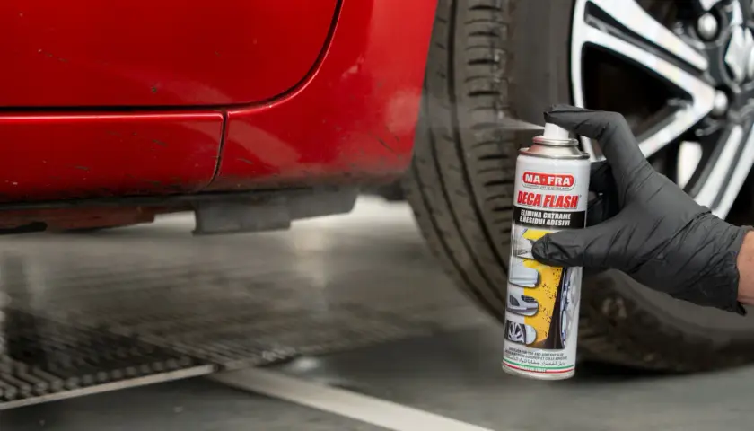 Guanto nero spruzza prodotto su auto rossa per togliere il catrame.