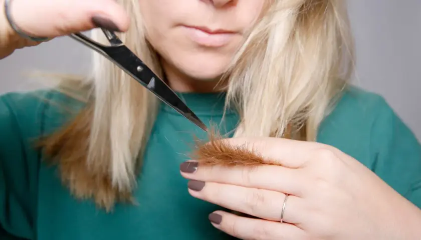 Kobieta z blond włosami podcina końcówki nożyczkami.