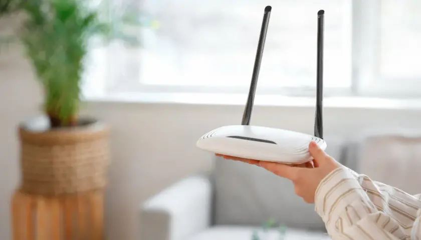 Dłoń trzyma biały router Wi-Fi z dwiema antenami. Może to być pomocne, gdy zastanawiasz się, jak zresetować urządzenie.