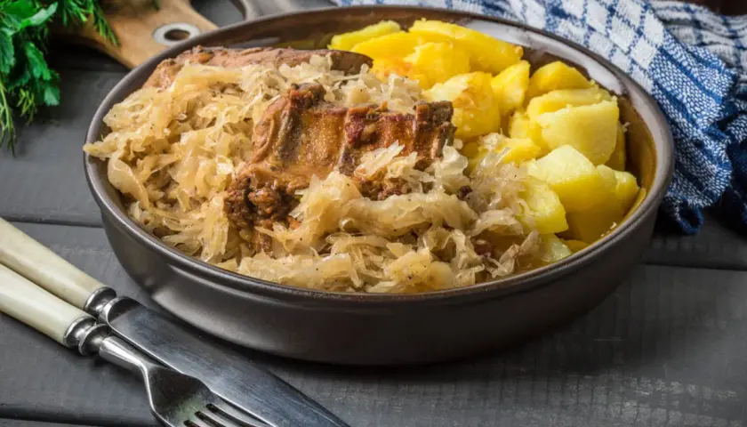 Pyszne żeberka w kapuście z ziemniakami. Danie podane w głębokim talerzu, obok sztućce.