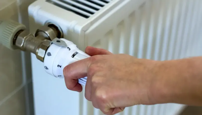 Dłoń reguluje termostat grzejnika, ustawiając temperaturę zgodnie z przepisami dotyczącymi minimalnej temperatury w mieszkaniu.