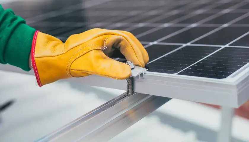 Ręka w żółtej rękawicy dokręca śrubę mocującą panel słoneczny. To ważny krok, by wiedzieć, jak dobrać falownik do instalacji.