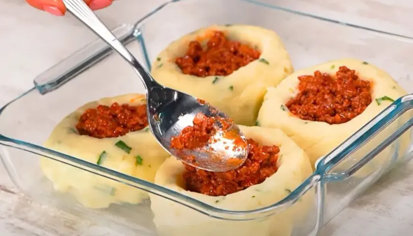 Łyżka nakłada mięsne nadzienie do ziemniaczanych łódeczek. Pyszne dania z ziemniaków w szklanym naczyniu.