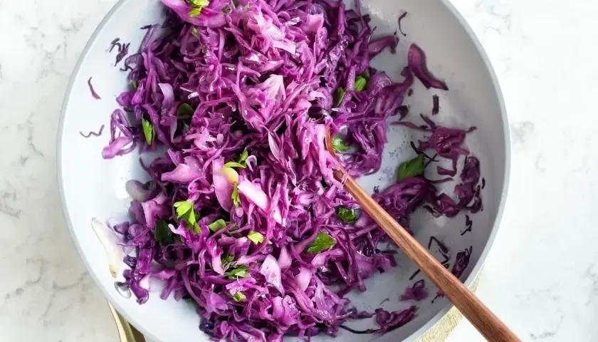 Insalata fresca di cavolo rosso, tagliato finemente e condito con erbe aromatiche, servita in una ciotola con un cucchiaio di legno.