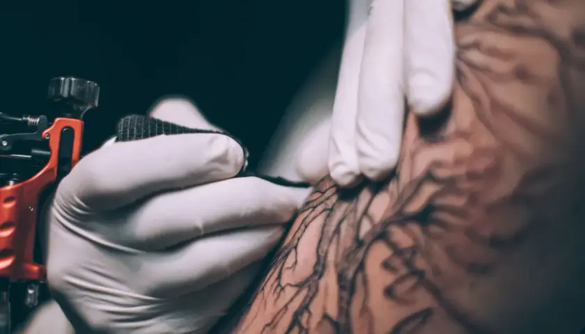 Dłoń w rękawiczce tworzy tatuaż metodą handpoke. To precyzyjne, ręczne tatuowanie, które daje unikalne efekty.