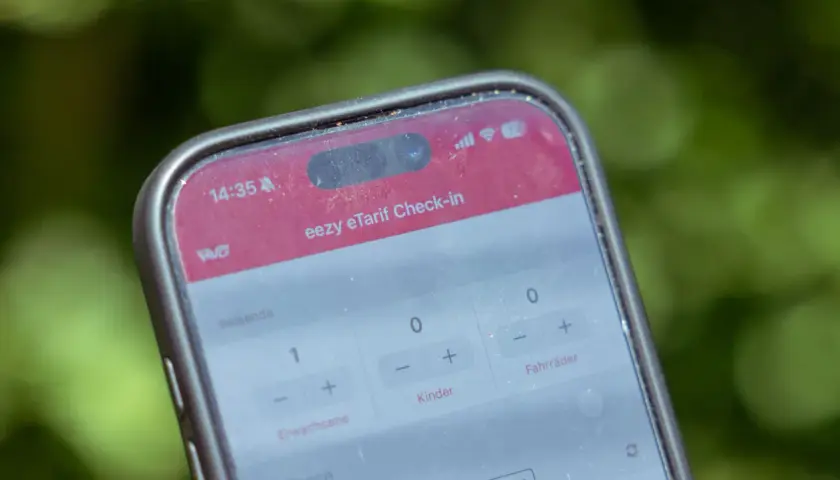 Ein Smartphone zeigt die "eezy eTarif Check-in" App. Ein Erwachsener und ein Kind sind für die Fahrt ausgewählt.