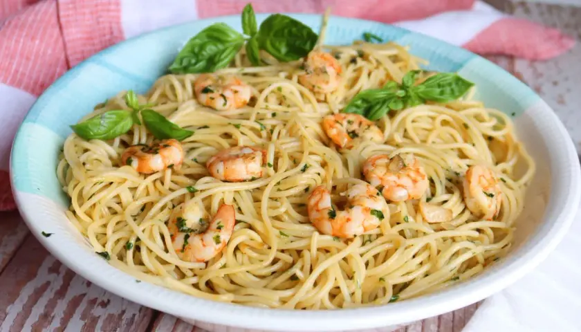 Un plato de espaguetis con gambas, adornado con hojas de albahaca fresca y perejil picado.