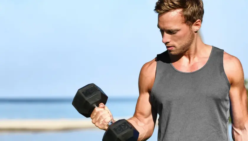 Mężczyzna ćwiczy biceps na świeżym powietrzu, podnosząc ciężarek. Zastanawia się, ile serii na biceps wykonać dzisiaj.