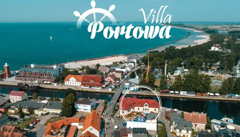 Widok z lotu ptaka na port i plażę w Darłówku. W centrum widoczny budynek z czerwonym dachem, otoczony kołem.