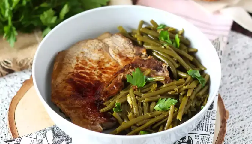 Une savoureuse côte de porc grillée accompagnée de haricots verts frais et persil, servie dans un bol blanc.