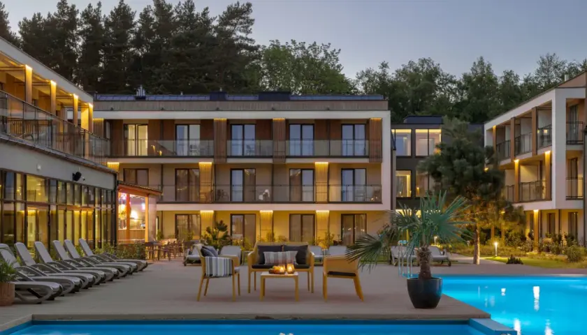 Relaks przy basenie w Saltic Resort & Spa. Nowoczesne budynki, leżaki i palmy tworzą idealne miejsce na wypoczynek.