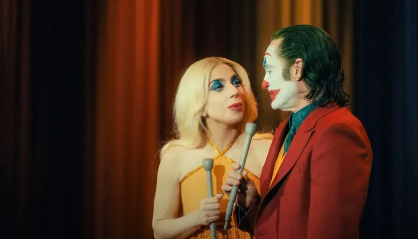 Joker e Harley Quinn, con microfoni in mano, si guardano intensamente. La trama del film si infittisce.